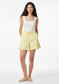 Balta kvadrātveida kakla tvertnes augšdaļa, kas saskaņota ar gaiši dzeltenām svītrainām šortiem. Šortiem ir elastīga jostasvieta un sānu kabatas.