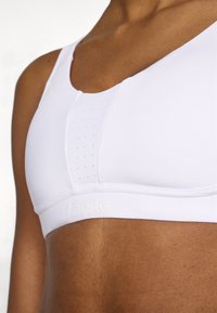Λευκό αθλητικό σουτιέν με ομαλή υφή, στρογγυλό λαιμόκομμα και λεπτομέρεια πανελ με τρύπες, με διακριτικό λογότυπο "BORG" στη ζώνη.