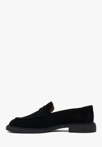 Schwarzer Wildleder-Slipper mit niedrigem Blockabsatz, abgerundeter Spitze und Riemendetail über dem Spann, im Profil vor weißem Hintergrund fotografiert.