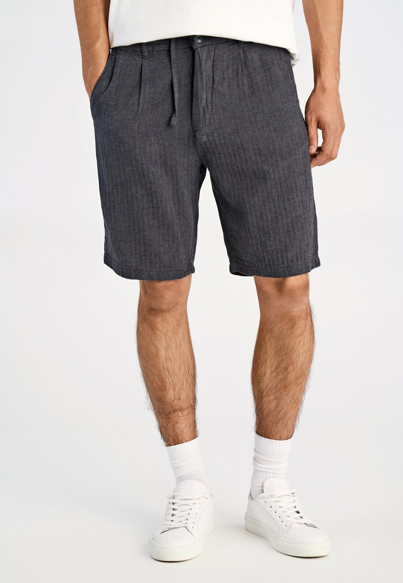 Mørkegrå shorts lavet af et tekstureret stof, med lodrette striber, justerbar talje og sidelommer, båret med hvide sneakers.