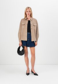 Beige knoopjasje met twee borstzakken, zwarte top, denim minirok, zwarte handtas en puntige kitten heels.