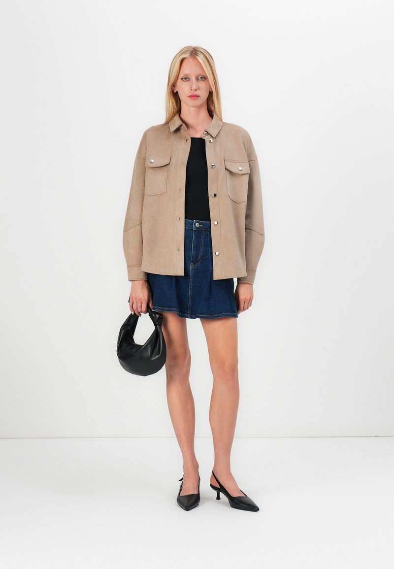 Giacca beige con bottoni, due tasche sul petto, top nero, mini gonna in denim, borsa nera e scarpe con tacco a spillo.