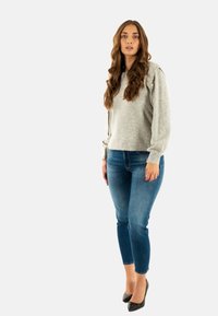 Maglione grigio a maglia con maniche lunghe, caratterizzato da dettagli con bottoni; abbinato a jeans skinny blu e tacchi alti neri. Outfit semplice e informale.