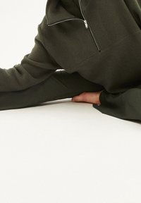 Pullover in pile verde scuro con zip frontale a quarti. Maniche lunghe e vestibilità comoda, caratterizzato da una superficie testurizzata e senza fantasie visibili.