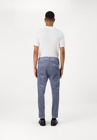 Pánská bílé žebrované tričko s krátkým rukávem kombinuje modré manšestrové kalhoty, má rovný střih a strukturovanou látku.