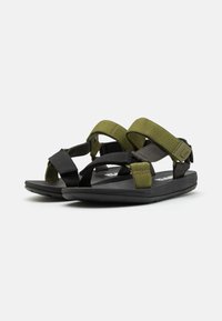 Sandalias en negro y verde oliva con correas ajustables, suelas de goma y plantilla acolchada, diseñadas para brindar comodidad y uso al aire libre.