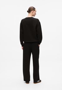 Sweatshirt preto em algodão com ombros caídos, combinado com calças correspondentes que apresentam detalhes com cravos na bainha e um corte descontraído.