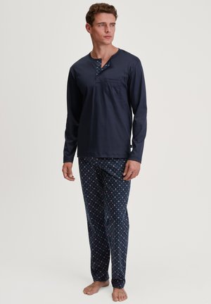 Marineblaue Langarm-Pyjama-Oberteil mit Henley-Ausschnitt und Tasche; gemusterte Hose in Marineblau mit roten und weißen geometrischen Designs.