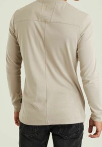 Beige long-sleeve shirt made of ribbed fabric, featuring a seam detail down the center back and small logo accent near the hem.