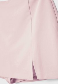 Svetloružový odev s vertikálnym švom a bočným rozparkom pri leme, vyrobený z hladkej, mierne textúrovanej látky.