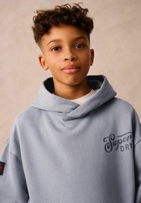 Lyseblå oversized hættetrøje med en blød tekstur, frontlomme og broderet "Superdry"-logo. Har en stor hætte og drop-skulder.