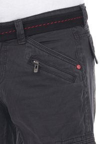 Schwarze Cargo-Hosen mit einer Reißverschlusstasche, strukturiertem Stoff und einem gewebten Bund mit roter Steppnaht und einem Logo-Button-Detail.
