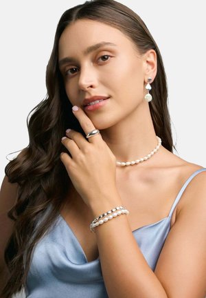 Set di gioielli in perle composto da un choker, orecchini e bracciale. Il choker e il bracciale presentano perle bianche rotonde; gli orecchini hanno un design a goccia con una grande perla.