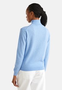 Hellblauer Pullover aus weichem Material, mit hohem Kragen und gerippten Bündchen. Das Design ist tailliert und betont die glatte Textur und Farbe.