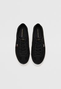 Paire de baskets en maille noire avec lacets, semelles blanches et petits drapeaux Tommy Hilfiger sur le côté sur un fond blanc uni.