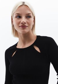 Top nero a costine con maniche lunghe, caratterizzato da dettagli con tagli sul colletto e una silhouette aderente. Tessuto morbido in tutta la sua lunghezza.