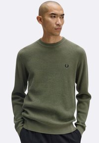 Maglione verde lavorato a maglia con un motivo testurizzato, collo rotondo e polsini e orlo a coste. Presenta un piccolo logo sul petto.
