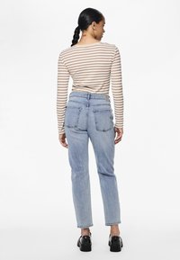 Haut à manches longues rayé aux couleurs beige et blanche, associé à un jean taille haute bleu clair. L'ensemble comprend des chaussures à plateforme noires.