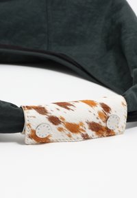 Zielona torba materiałowa z teksturowanym, wzorzystym białym i brązowym paskiem z futra oraz metalowymi akcentami. Charakteryzuje się miękkim, gładkim designem i trwałymi materiałami.