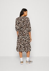 Leopardmønstret kjole med korte pufærmer, bånd i taljen og volangkant. Materialet virker let; bæres med sneakers og sokker.