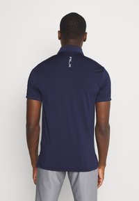 Mörkblå polo med krage, korta ärmar och RLX-logotyp i vitt på baksidan. Släthet, lätt tyg med en figurnära design.