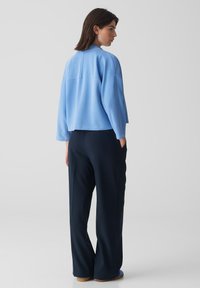 Veste courte bleu clair avec un col rond, des manches amples et une coupe droite, associée à un pantalon large bleu marine. Texture lisse.