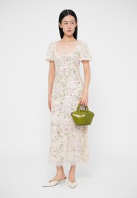 Krémové maxi šaty s výšivkou kvetov a flitrami, s krátkymi nariasenými rukávmi a štvorcovým výstrihom, doplnené zelenou kabelkou a bielymi sandálmi.