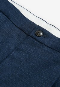 Pantalones ajustados de color azul marino, confeccionados en una tela texturizada con un cierre de botón visible, que cuentan con un forro blanco contrastante y patrones sutiles.