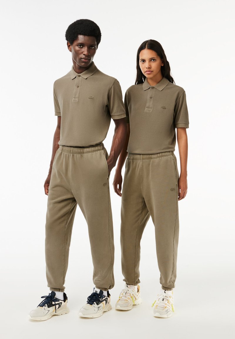 Olivgrüne Poloshirts und Sweatpants mit entspannter Passform, gerippten Details und Logo-Akzenten. Dazu passend werden legere Schuhe getragen.