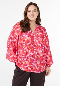 Jasno kolorowa bluzka z długim rękawem, zdobiona kwiecistym wzorem w odcieniach różu i pomarańczy, z dekoltem w kształcie litery V oraz marszczeniem przy dekolcie.