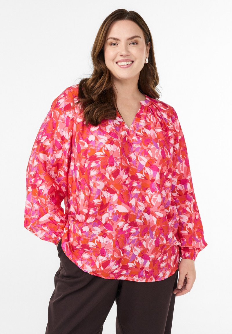 Jasno kolorowa bluzka z długim rękawem, zdobiona kwiecistym wzorem w odcieniach różu i pomarańczy, z dekoltem w kształcie litery V oraz marszczeniem przy dekolcie.