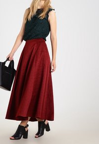 Falda A de línea roja, texturizada y de cintura alta, combinada con una blusa a rayas de color verde oscuro. Unos tacones negros abiertos y un bolso negro completan el conjunto.