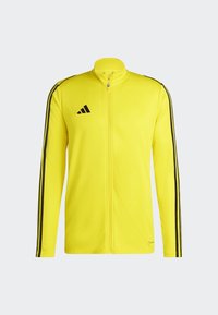 Gelbe Zip-Jacke mit schwarzen Akzenten und drei schwarzen Streifen entlang der Ärmel. Hergestellt aus glattem Stoff, mit Stehkragen.