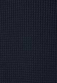 Gros plan sur un tissu tricoté bleu foncé avec une texture côtelée verticale et des fibres de fil doux visibles.