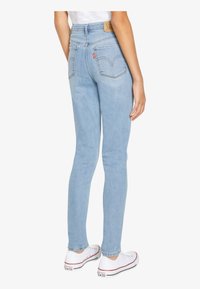 Light blue high-waisted jeans with back pockets featuring stitched design, paired with white sneakers. Denim texture visible.