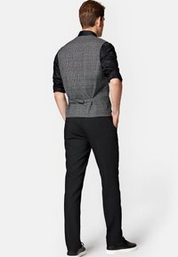 Szary kamizelka w kratę z czarną koszulą pod spodem, zestawiona z czarnymi spodniami i sneakersami. Widok z tyłu ukazuje subtelny detal regulacji w talii.