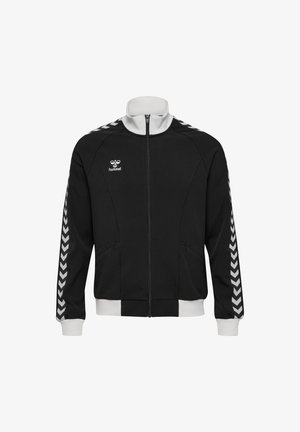 Schwarze Sportjacke mit Reißverschluss, weißen Chevron-Streifen an den Ärmeln, weißem Kragen und Bündchen sowie kleinem "hummel"-Logo auf der Brust.