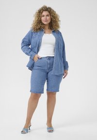 Set din cămașă din denim cu dungi și pantaloni scurți în albastru deschis, având nasturi, un buzunar și detalii destrămate pe pantaloni scurți, asortat cu sandale cu toc albastre.