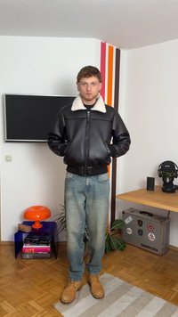 Casaco bomber de couro preto com colarinho de pelo sintético branco, fecho éclair frontal e punhos canelados, combinado com jeans de denim azul e botas bege.