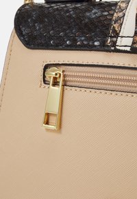 Beżowa torebka z fakturowaną powierzchnią, czarną klapą w wężowy wzór oraz złotym suwakiem z kwadratowym wycięciem.