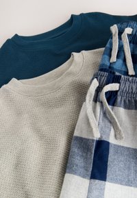 Kolm rõivaeset: tume teilsinine tekstuuriga kampsun, helehalli võrkudega kampsun ja mustrilised sinise-valge ruudulised lühikesed püksid nööriga.