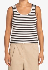 Černobíle pruhovaný tílko s žebrovanou texturou, s výstřihem do kulata a ramínky. V kombinaci s béžovými kalhotami s vysokým pasem.