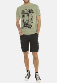 T-shirt en coton vert avec impression graphique noire de moto et de palmiers, associé à un short cargo noir avec poches latérales et ourlets retroussés.