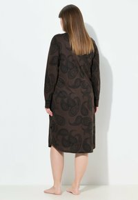 Vestido largo marrón con patrón de paisley negro, de mangas largas y con aberturas en los costados. Hecho de tejido suave, diseñado para caer por debajo de la rodilla.