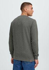 Grå langermet genser med rund hals og ribbede mansjetter, med et lite logomerke ved kanten og et strukturert tekstildesign.