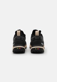 Schwarze Outdoorschuhe mit beiger Sohle, strukturiertem Absatz und buntem Akzent auf der Rückseite. Verfügt über verstärkte Ösen und eine Zuglasche.