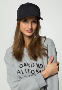 Sort baseball cap med en struktureret design, kombineret med en lysegrå sweatshirt med en sort trykt tekstdesign.