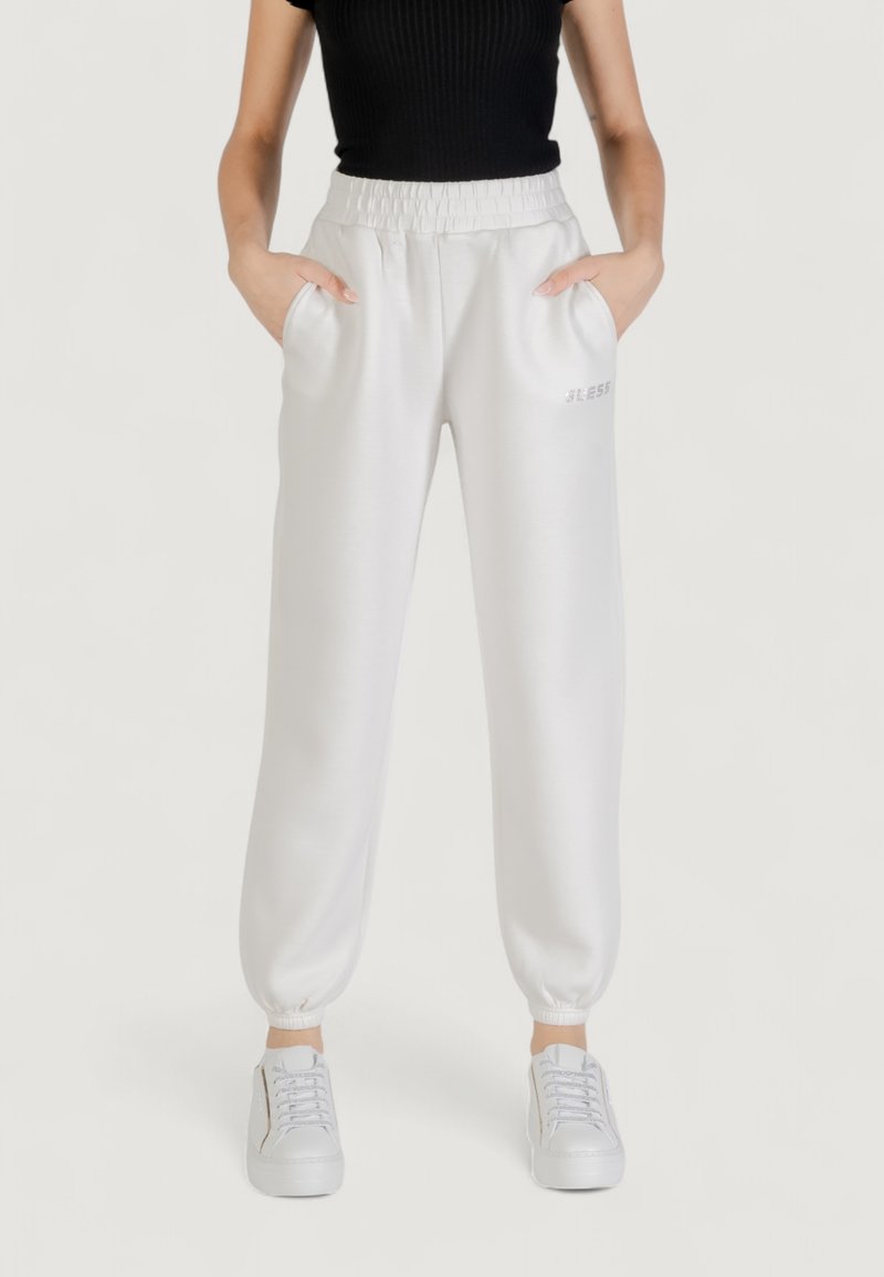 Pantaloni della tuta bianchi con una cintura a coste, polsini elastici, tasche laterali e un discreto marchio "BLESS" in testo chiaro. Abbinati a scarpe bianche.