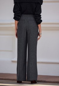 Grau melierte Hosen mit weitem Bein aus einem strukturierten Wollmischgewebe, mit hohem Bund und zwei Gesäßtaschen, kombiniert mit einem dunklen Pullover.