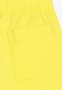 Žluté bavlněné šortky s elastickým pasem a náprsní kapsou na zadní straně, které se vyznačují hladkou texturou a jasnou barvou.